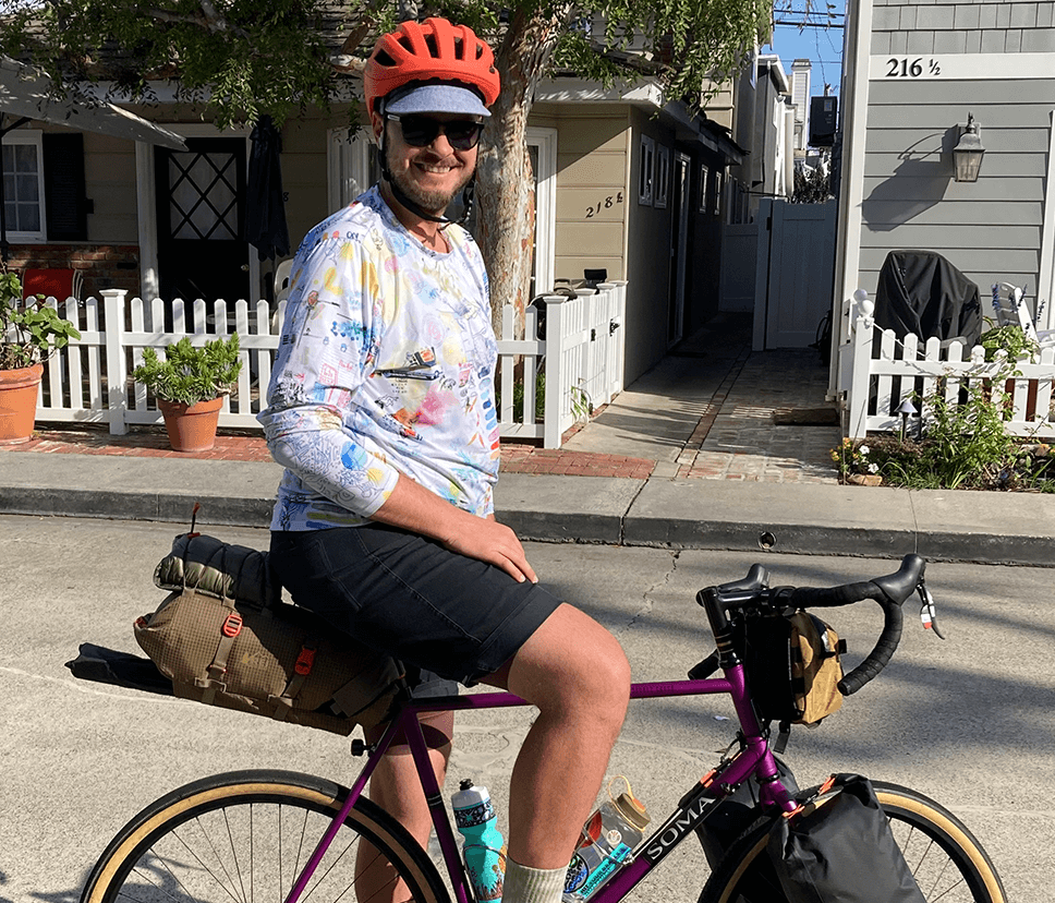 A cropped image of Spenser Williams on his purple road bike, smiling for the camera for our About Us page.