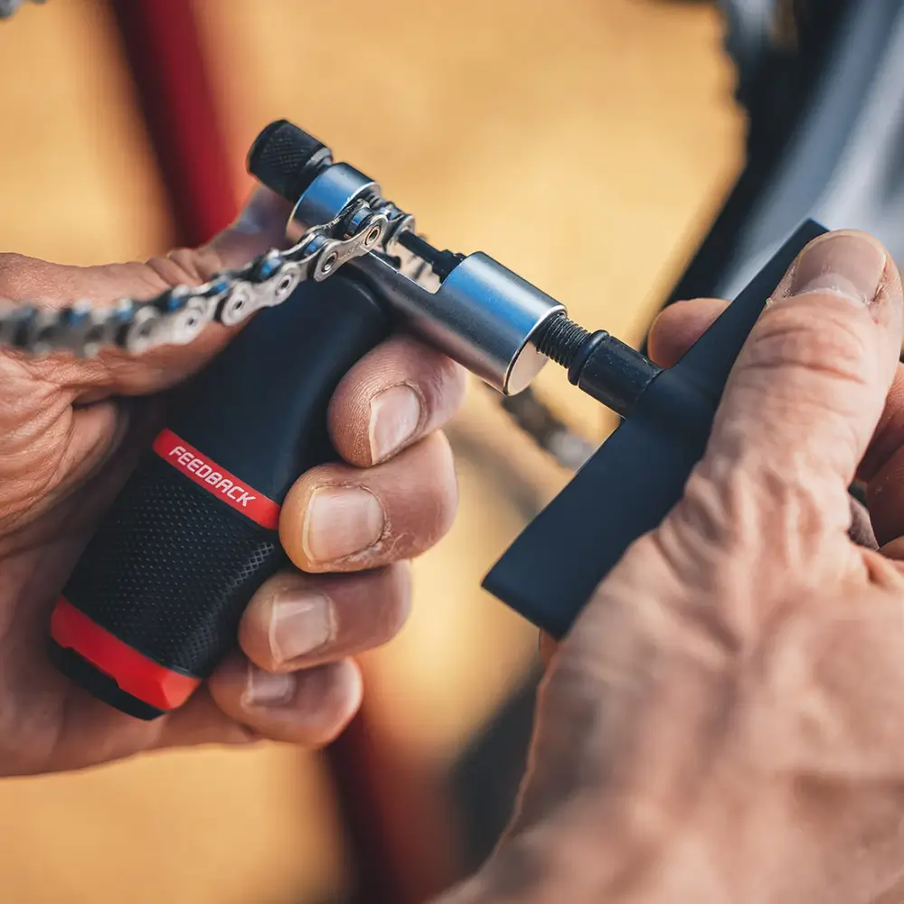 A black and red Feedback Sports Chain Tool 3.0 being used on a chain.