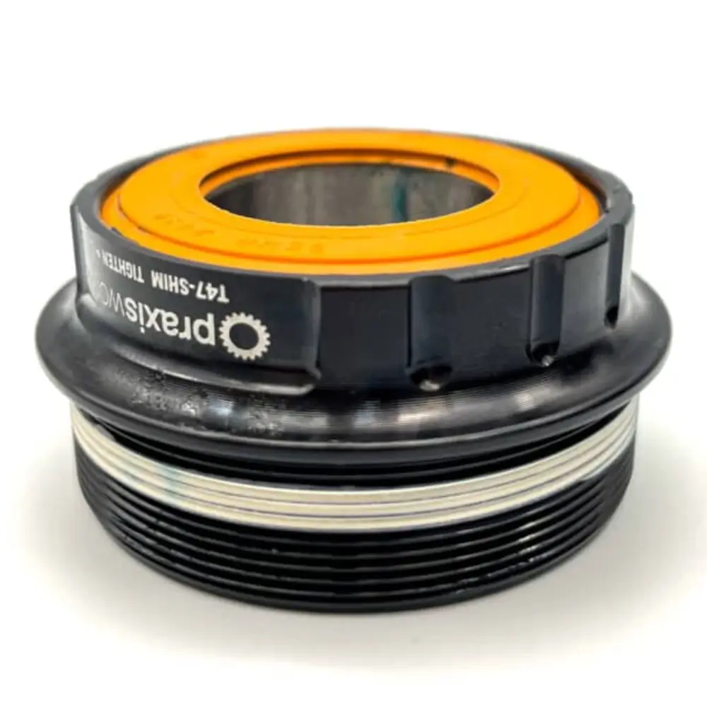 An orange Praxis 24MM Bottom Bracket Seal Kit installed on a single side of a Praxis bottom bracket